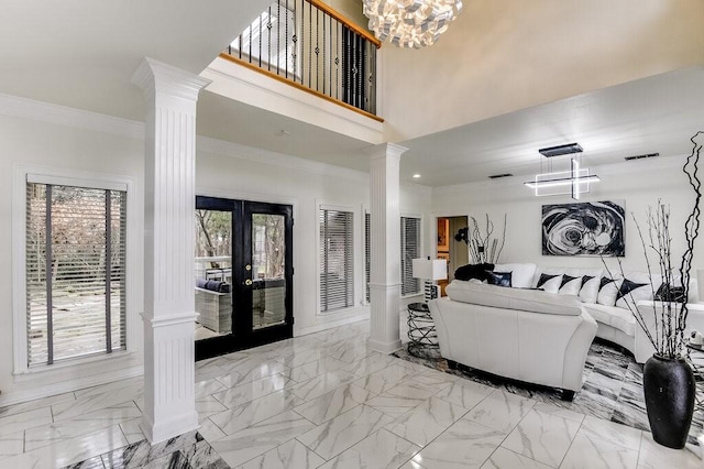 living room with a towering ceiling, decorative columns, a notable chandelier, ornamental molding, and french doors