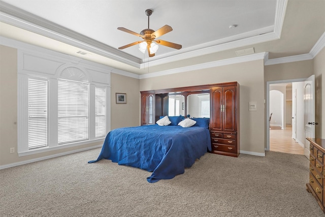 carpeted bedroom with crown molding, a tray ceiling, and multiple windows