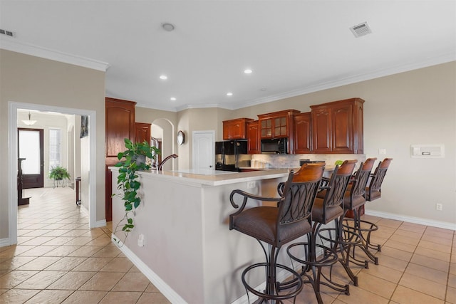 kitchen featuring a kitchen breakfast bar, decorative backsplash, light tile patterned floors, black appliances, and crown molding