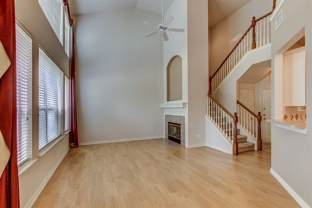 unfurnished living room featuring ceiling fan, a towering ceiling, a tiled fireplace, and light hardwood / wood-style flooring