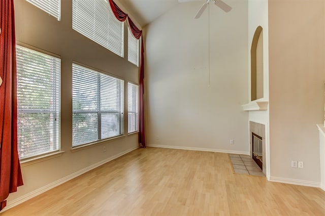 unfurnished living room with a tiled fireplace, light wood-type flooring, ceiling fan, and a towering ceiling