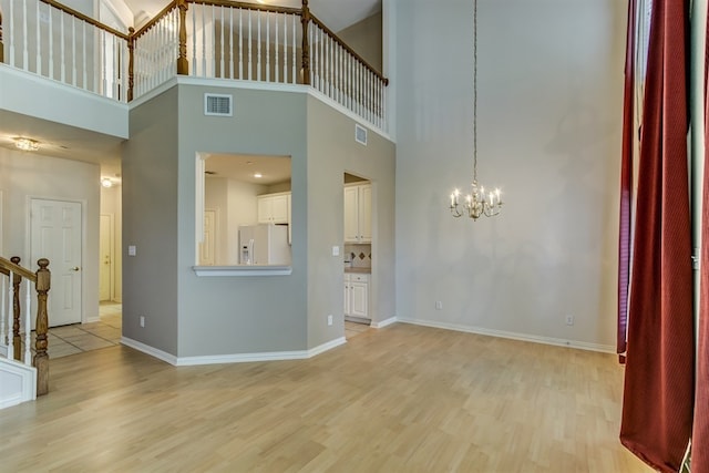 unfurnished living room with a towering ceiling, a chandelier, and light hardwood / wood-style flooring