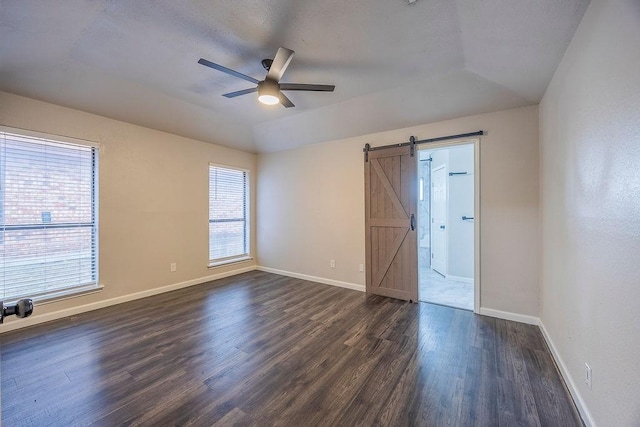 unfurnished room with dark hardwood / wood-style flooring, vaulted ceiling, a barn door, and ceiling fan