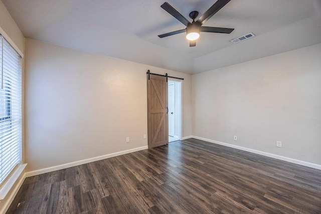 empty room featuring dark hardwood / wood-style flooring, vaulted ceiling, a barn door, and ceiling fan