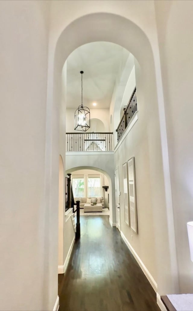 hall with dark wood-type flooring, a chandelier, and a towering ceiling