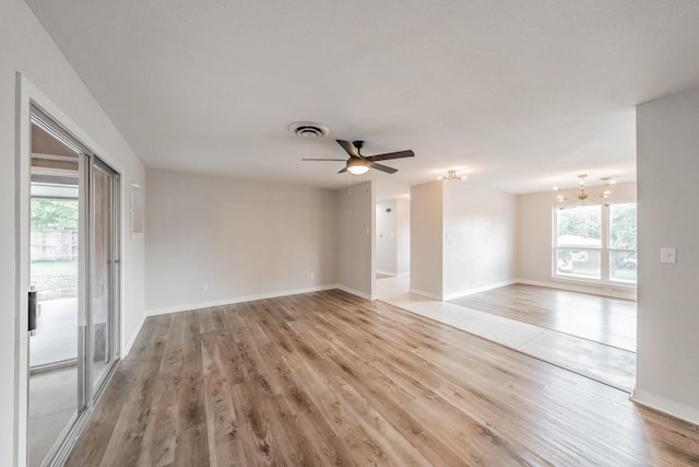 unfurnished room featuring ceiling fan with notable chandelier, light wood-type flooring, and a wealth of natural light