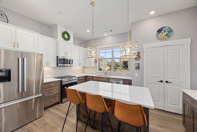 kitchen with white cabinetry, hanging light fixtures, stainless steel appliances, a center island, and light hardwood / wood-style floors