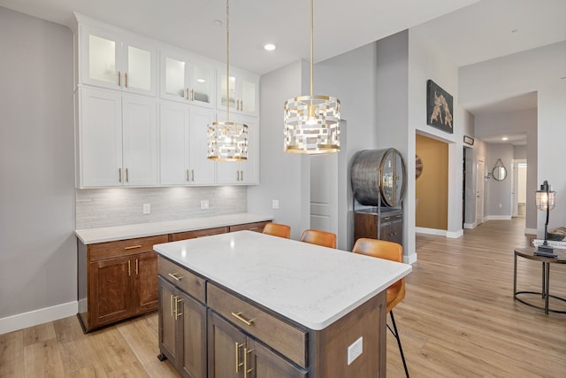 kitchen with a kitchen island, backsplash, white cabinets, a kitchen bar, and light hardwood / wood-style floors