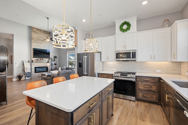 kitchen featuring a kitchen bar, a center island, appliances with stainless steel finishes, pendant lighting, and white cabinets