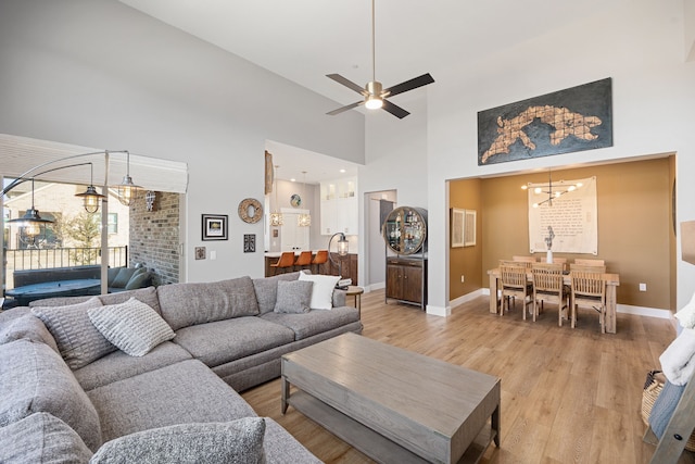 living room featuring a towering ceiling, ceiling fan with notable chandelier, and light wood-type flooring