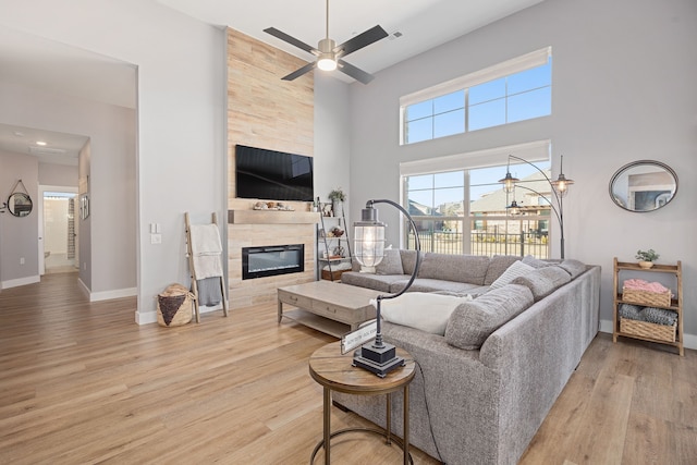 living room featuring a tiled fireplace, a towering ceiling, ceiling fan, and light wood-type flooring