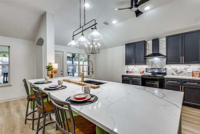 kitchen featuring light stone counters, wall chimney range hood, electric range, and sink