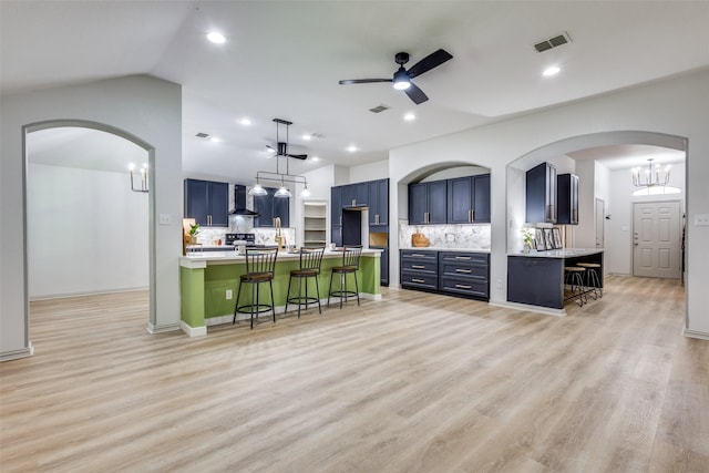 kitchen featuring decorative light fixtures, blue cabinets, a breakfast bar area, a center island, and wall chimney range hood