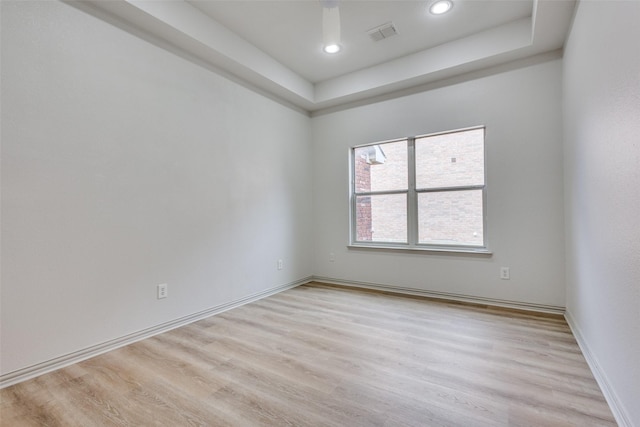 empty room with light wood-type flooring and a tray ceiling