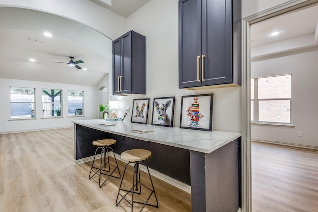 kitchen with light hardwood / wood-style flooring, ceiling fan, light stone counters, a kitchen bar, and vaulted ceiling