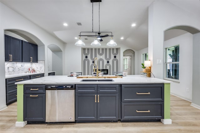 kitchen featuring sink, hanging light fixtures, stainless steel dishwasher, light stone countertops, and a kitchen island with sink