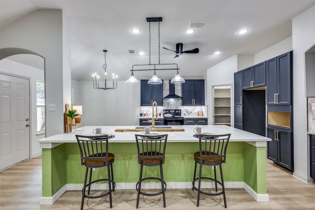 kitchen with wall chimney range hood, a center island with sink, a breakfast bar area, and black / electric stove