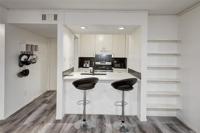 kitchen featuring a breakfast bar area, white cabinetry, decorative backsplash, stainless steel electric stove, and kitchen peninsula