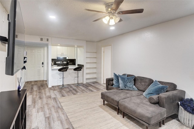 living room featuring ceiling fan, a textured ceiling, and light hardwood / wood-style flooring