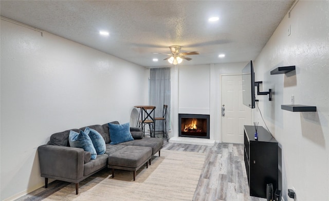 living room featuring ceiling fan, light hardwood / wood-style floors, and a textured ceiling