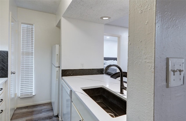 kitchen with sink, white appliances, white cabinetry, hardwood / wood-style floors, and a textured ceiling