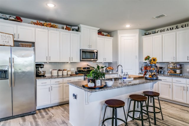 kitchen with white cabinetry, appliances with stainless steel finishes, an island with sink, and dark stone counters