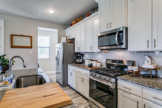 kitchen with appliances with stainless steel finishes, sink, dark stone countertops, white cabinets, and decorative backsplash