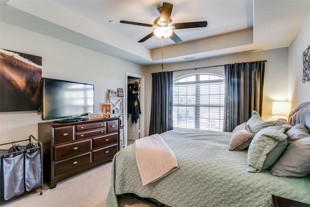 bedroom featuring ceiling fan, a tray ceiling, a walk in closet, light colored carpet, and a closet