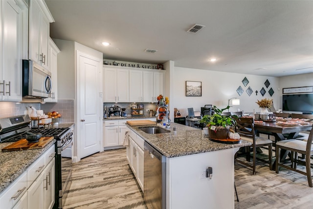 kitchen featuring sink, stone counters, stainless steel appliances, an island with sink, and white cabinets