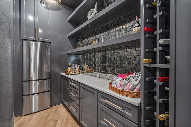 bar featuring light wood-type flooring, stainless steel fridge, gray cabinets, light stone countertops, and decorative backsplash