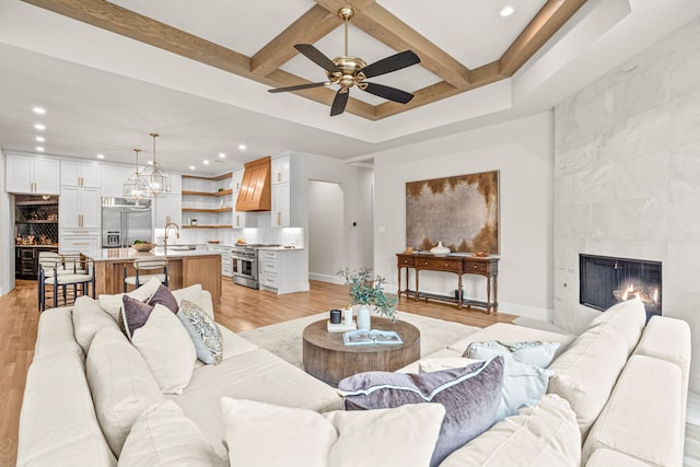 living room with beamed ceiling, sink, a tiled fireplace, coffered ceiling, and light hardwood / wood-style floors