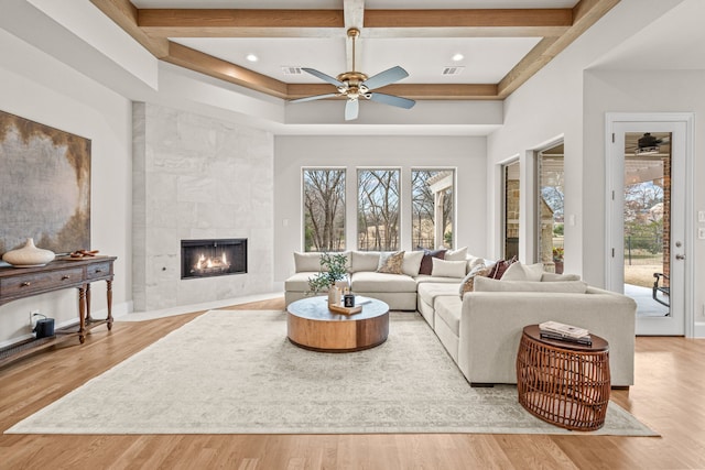 living room featuring beamed ceiling, ceiling fan, a tiled fireplace, and light hardwood / wood-style floors