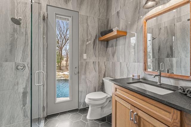 bathroom featuring a shower with door, tile walls, vanity, tile patterned floors, and toilet