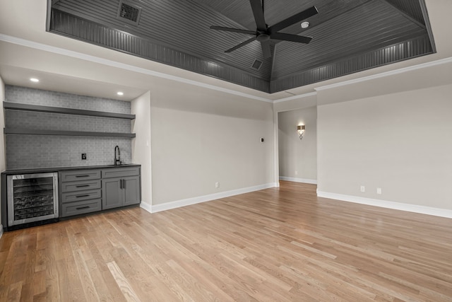 interior space with ceiling fan, ornamental molding, wet bar, beverage cooler, and light wood-type flooring