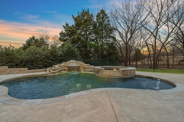 pool at dusk with an in ground hot tub, pool water feature, and a patio