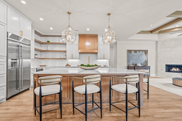 kitchen featuring white cabinetry, built in refrigerator, a large island, and hanging light fixtures