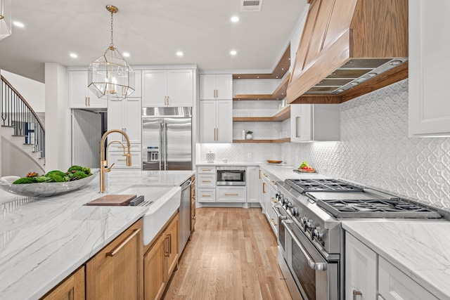 kitchen with white cabinetry, built in appliances, light stone counters, and hanging light fixtures