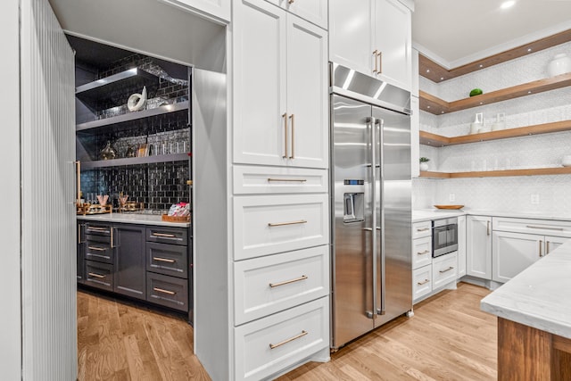 kitchen featuring built in refrigerator, light stone counters, white cabinets, and light wood-type flooring