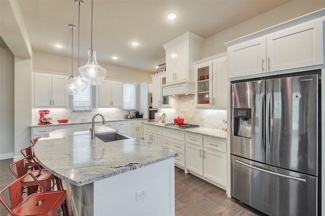 kitchen featuring appliances with stainless steel finishes, sink, white cabinets, hanging light fixtures, and a kitchen island with sink