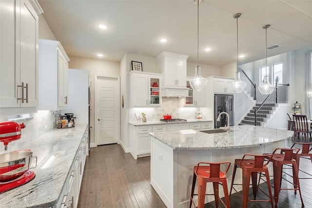 kitchen with hanging light fixtures, white cabinetry, a kitchen island with sink, and sink