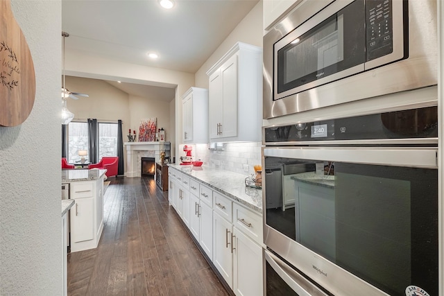 kitchen with appliances with stainless steel finishes, dark hardwood / wood-style floors, light stone countertops, and white cabinets