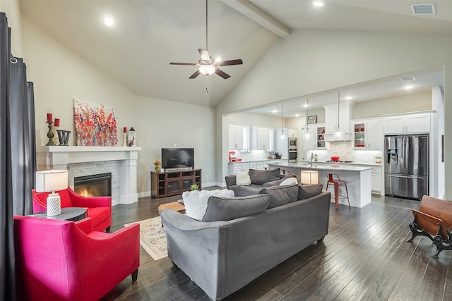 living room featuring dark hardwood / wood-style floors, high vaulted ceiling, a fireplace, beamed ceiling, and ceiling fan