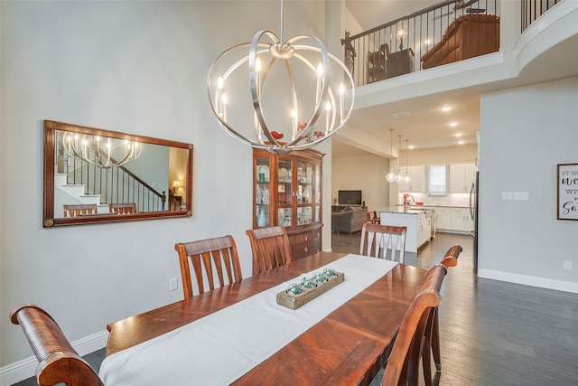 dining space featuring baseboards, wood finished floors, a towering ceiling, and a notable chandelier