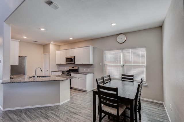 kitchen with sink, kitchen peninsula, stainless steel appliances, light stone countertops, and white cabinets