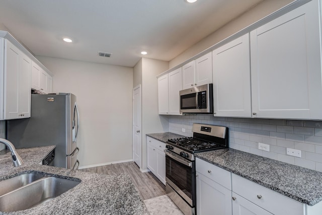 kitchen featuring sink, stainless steel appliances, tasteful backsplash, white cabinets, and dark stone counters