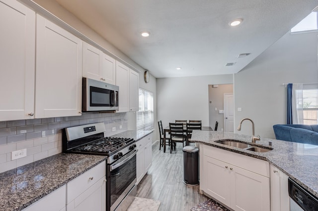 kitchen with stone counters, appliances with stainless steel finishes, white cabinetry, sink, and backsplash