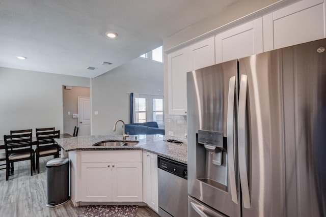 kitchen with sink, stainless steel appliances, light stone counters, white cabinets, and kitchen peninsula