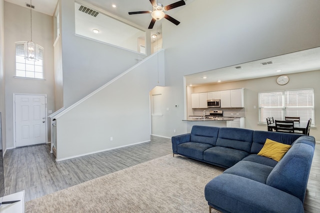 living room with a towering ceiling, sink, ceiling fan with notable chandelier, and light hardwood / wood-style flooring