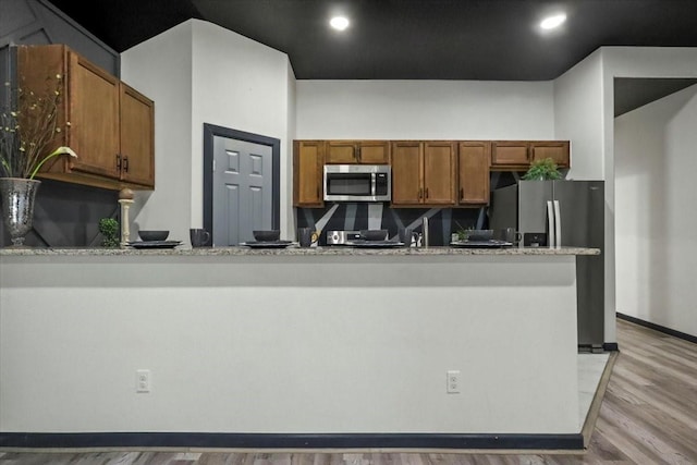 kitchen with light stone counters, sink, stainless steel appliances, and light hardwood / wood-style floors