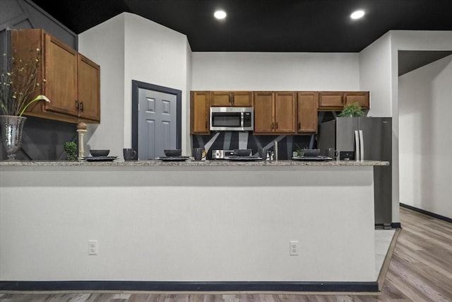 kitchen with light stone countertops, appliances with stainless steel finishes, and light wood-type flooring